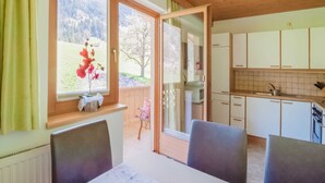 A room with a dining table, chairs, a window with a view of mountains, and a kitchen area with cabinets and a sink. - Apartment With Panoramic View (Ramsau im Zillertal)