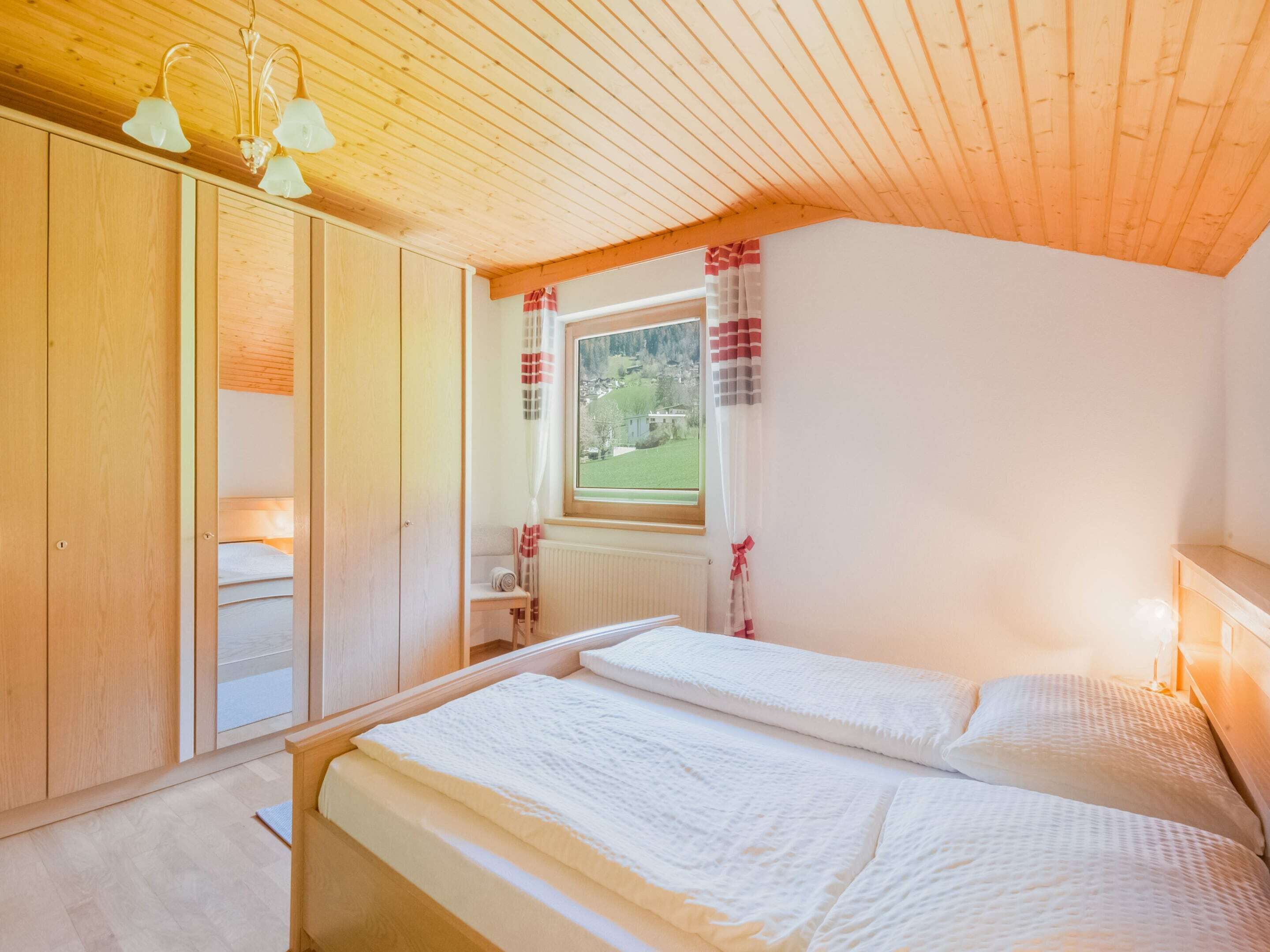 A bedroom with two beds, wooden ceiling, and a window with curtains.