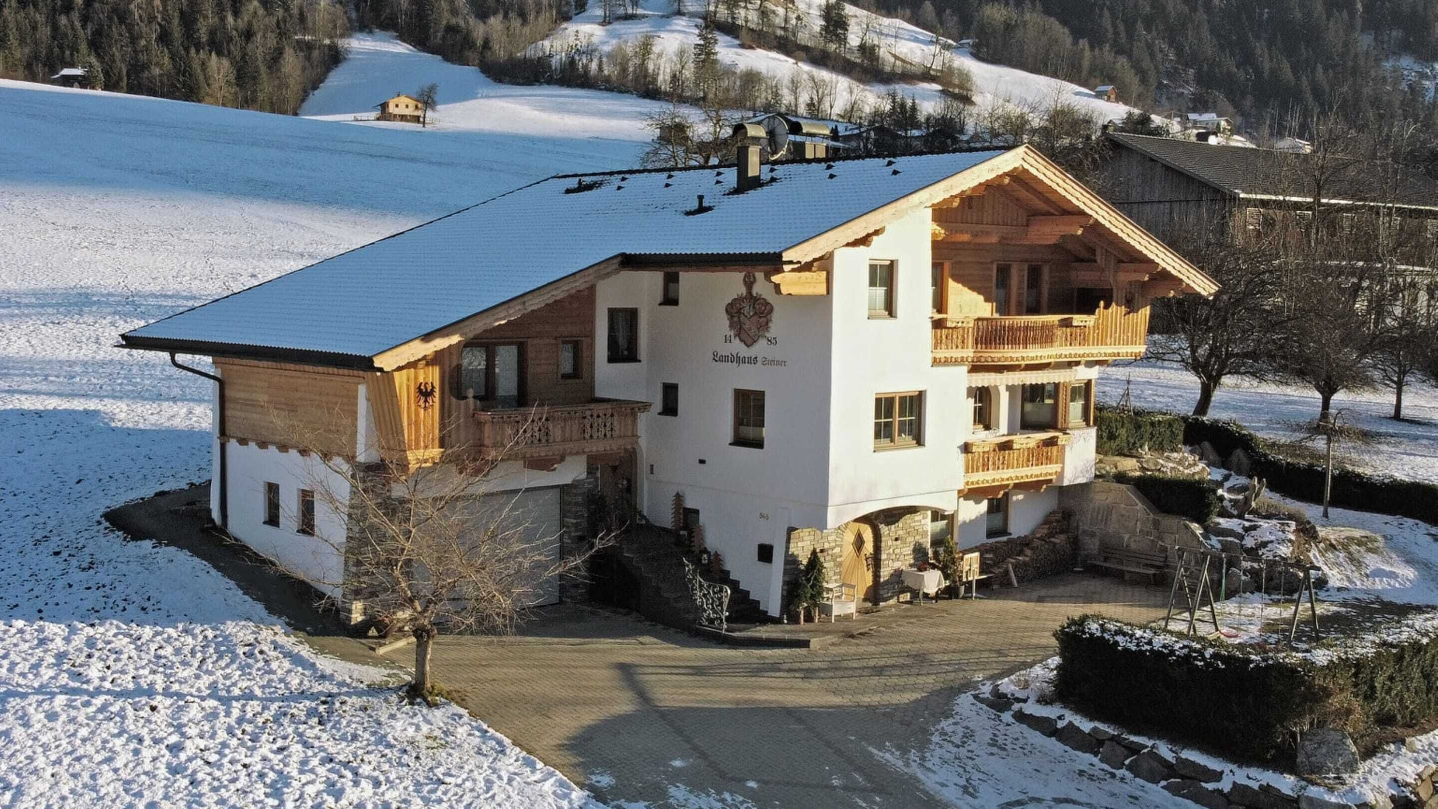 Een traditioneel gebouw in Alpenstijl met een balkon, een stenen fundering en een besneeerd landschap.