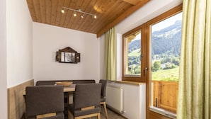 A dining area with a wooden table and chairs, a window with a view of a mountainous landscape, and a wooden ceiling with recessed lighting. - Apartment With Panoramic View (Ramsau im Zillertal)