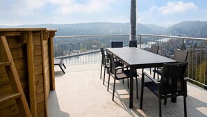 A balcony with a table and chairs, overlooking a river and cityscape. - Holiday Home in HUY Near Town Center (Wanze)