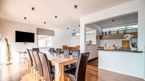 A modern dining area with a wooden table and chairs, a kitchen with a bar area, and a television mounted on the wall. - Holiday Home in HUY Near Town Center (Wanze)