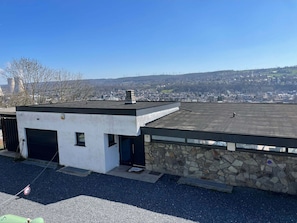 Ein modernes Gebäude mit flachem Dach, einer Steinsäule und freiem Blick auf eine Stadt im Hintergrund.