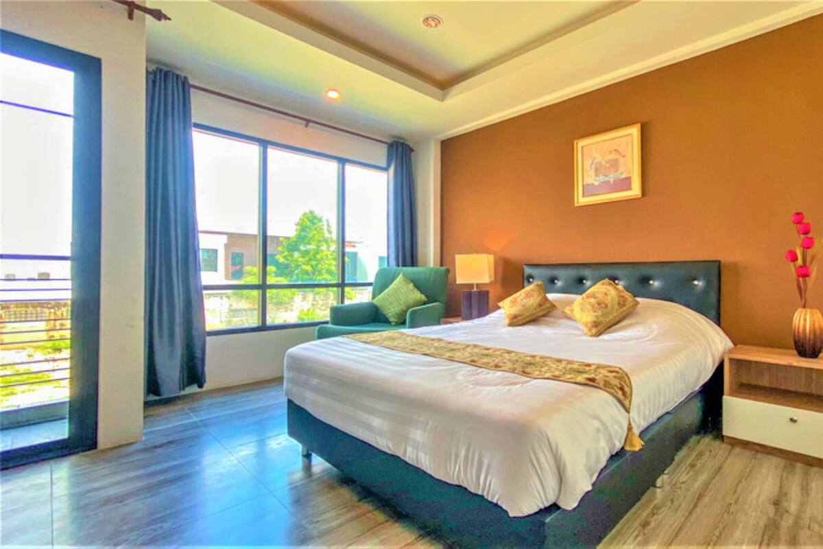 A hotel room with a large bed, a nightstand, a chair, a window with curtains, and a vase with flowers.
