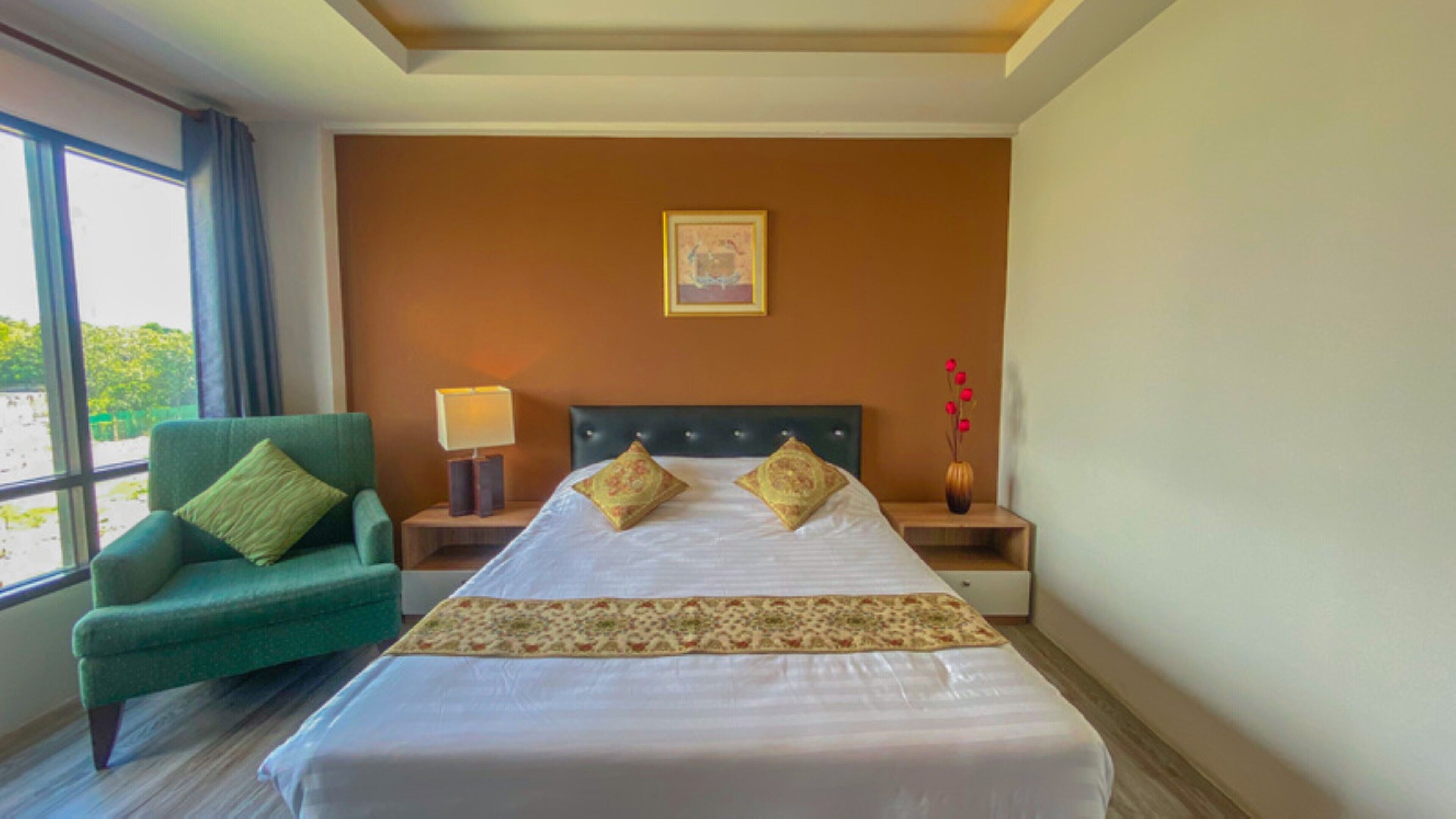 A hotel room with a large bed, a green armchair, a nightstand with a lamp, and a framed picture on the wall.