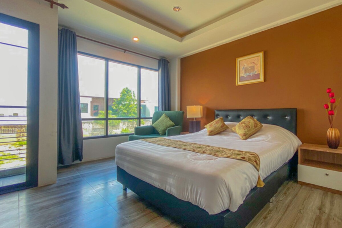 A hotel room with a large bed, a nightstand, a chair, a window with a view, and a painting on the wall.