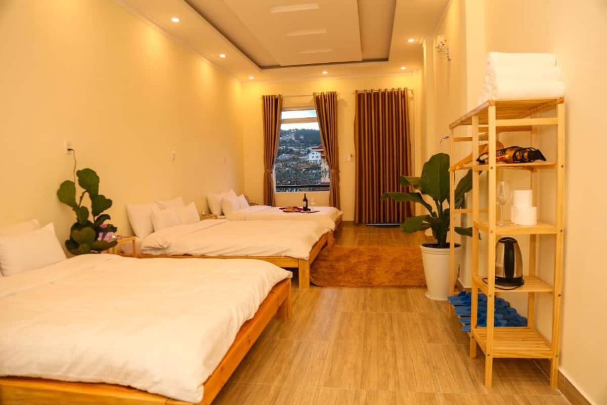 A hotel room with two beds, a wooden shelf with towels, a potted plant, and a view of a snowy landscape through the window.