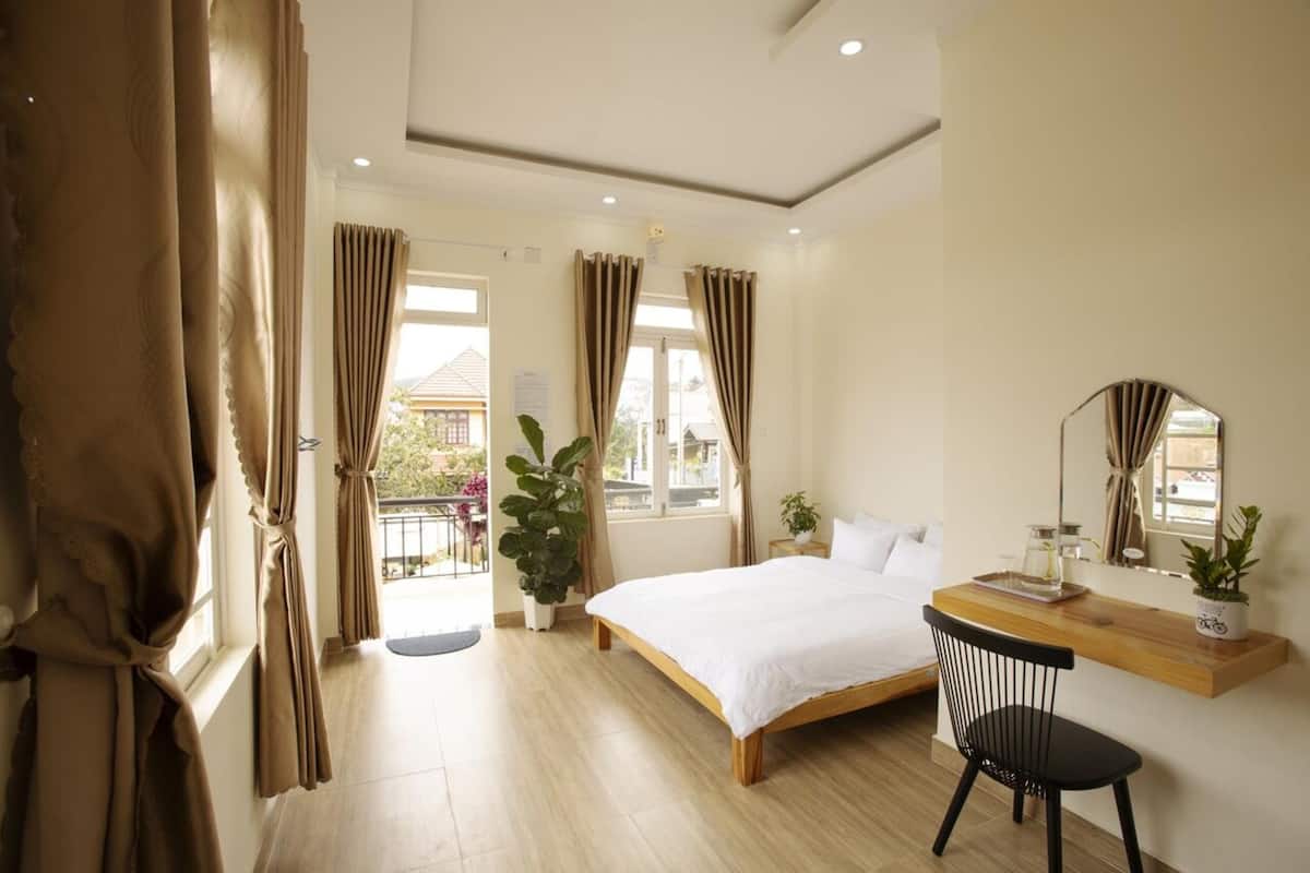 A bedroom with a bed, a desk, a chair, a mirror, and a balcony with curtains.