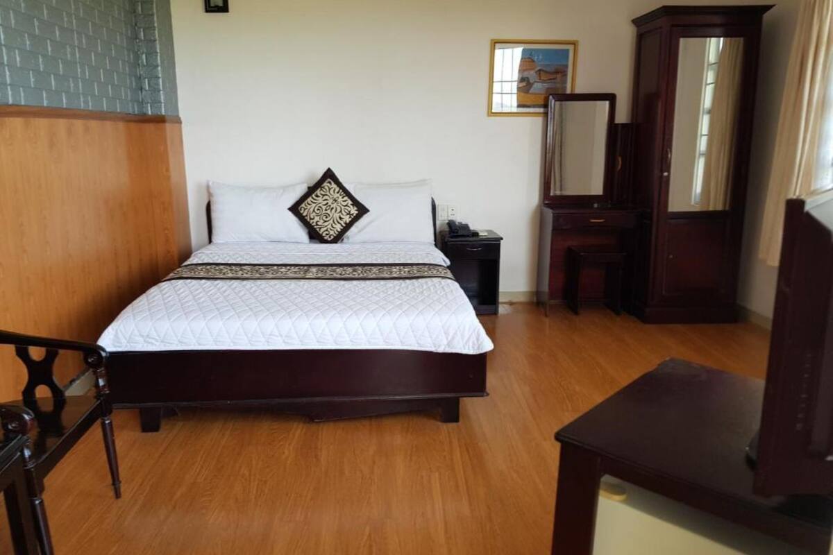 A neatly arranged bedroom with a large bed, a wooden nightstand, a dresser, and a mirror.