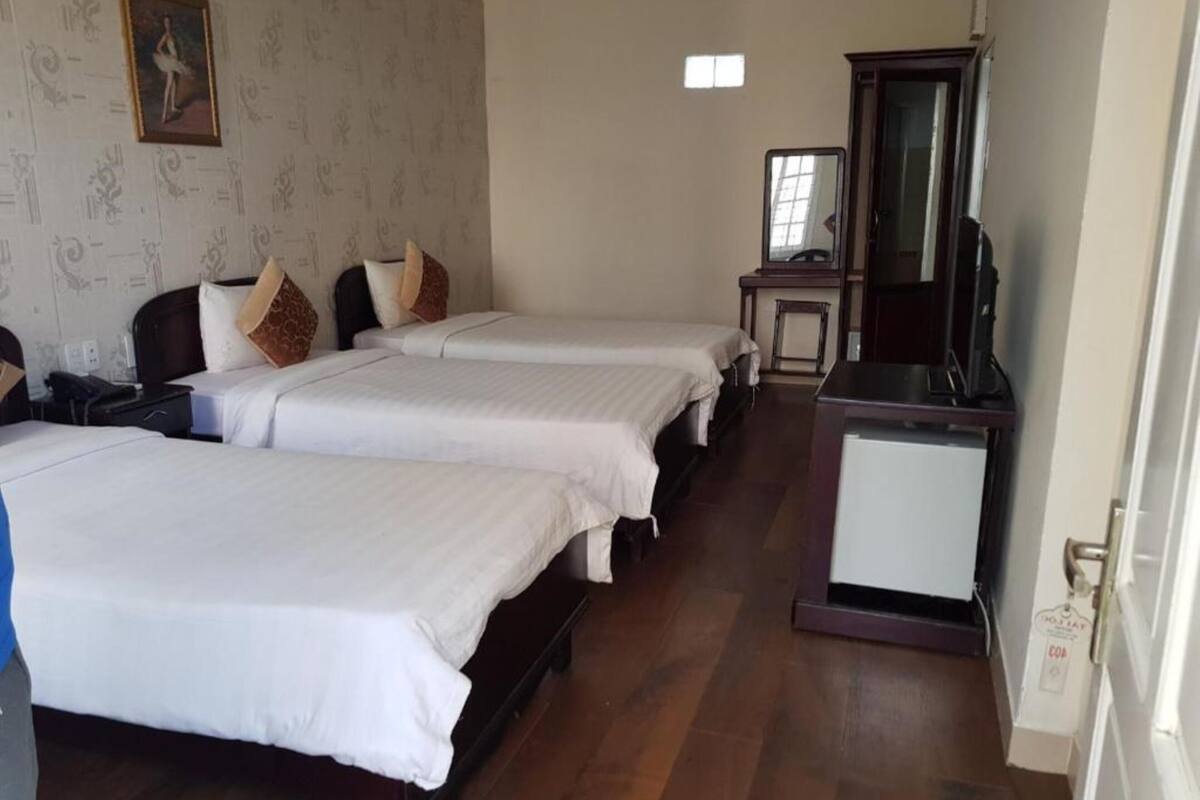 A hotel room with two beds, a desk, a small cabinet, and a mirror.