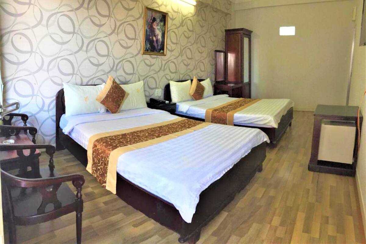 A hotel room with two beds, a wooden chair, a desk, and a cabinet.