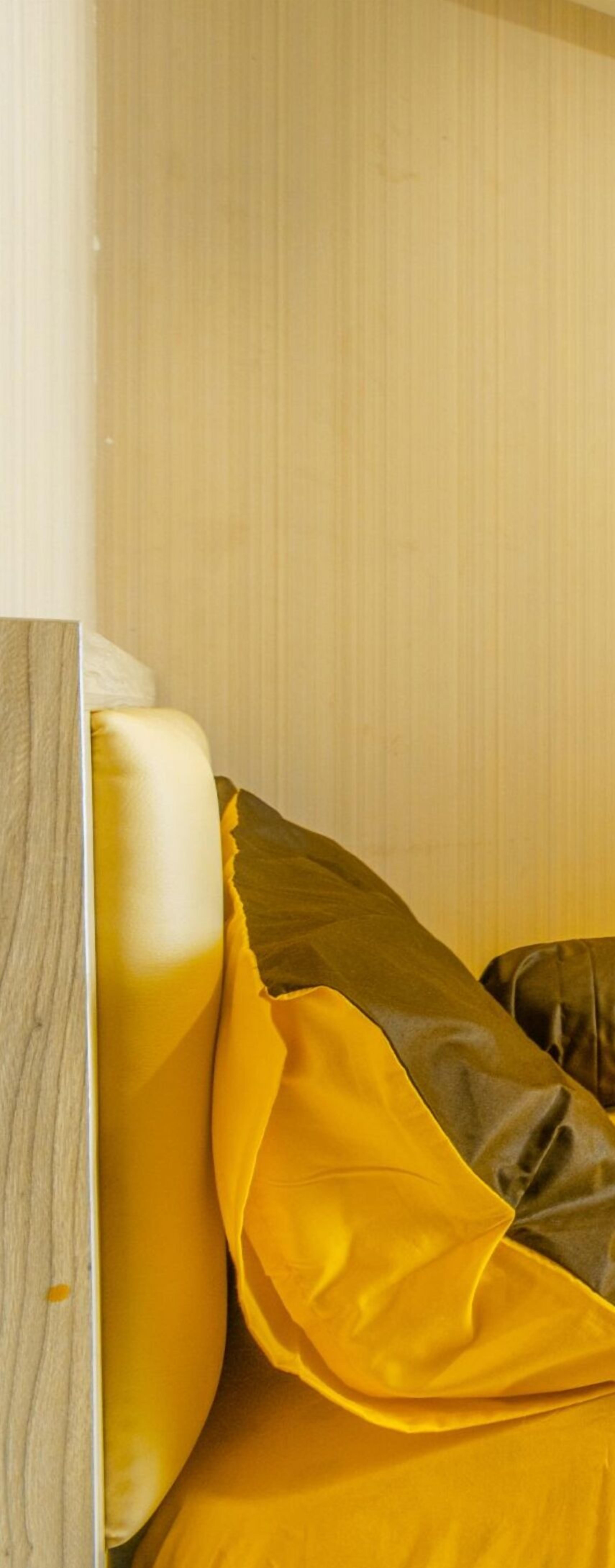 A corner of a room with a wooden headboard and a yellow fabric draped over it.