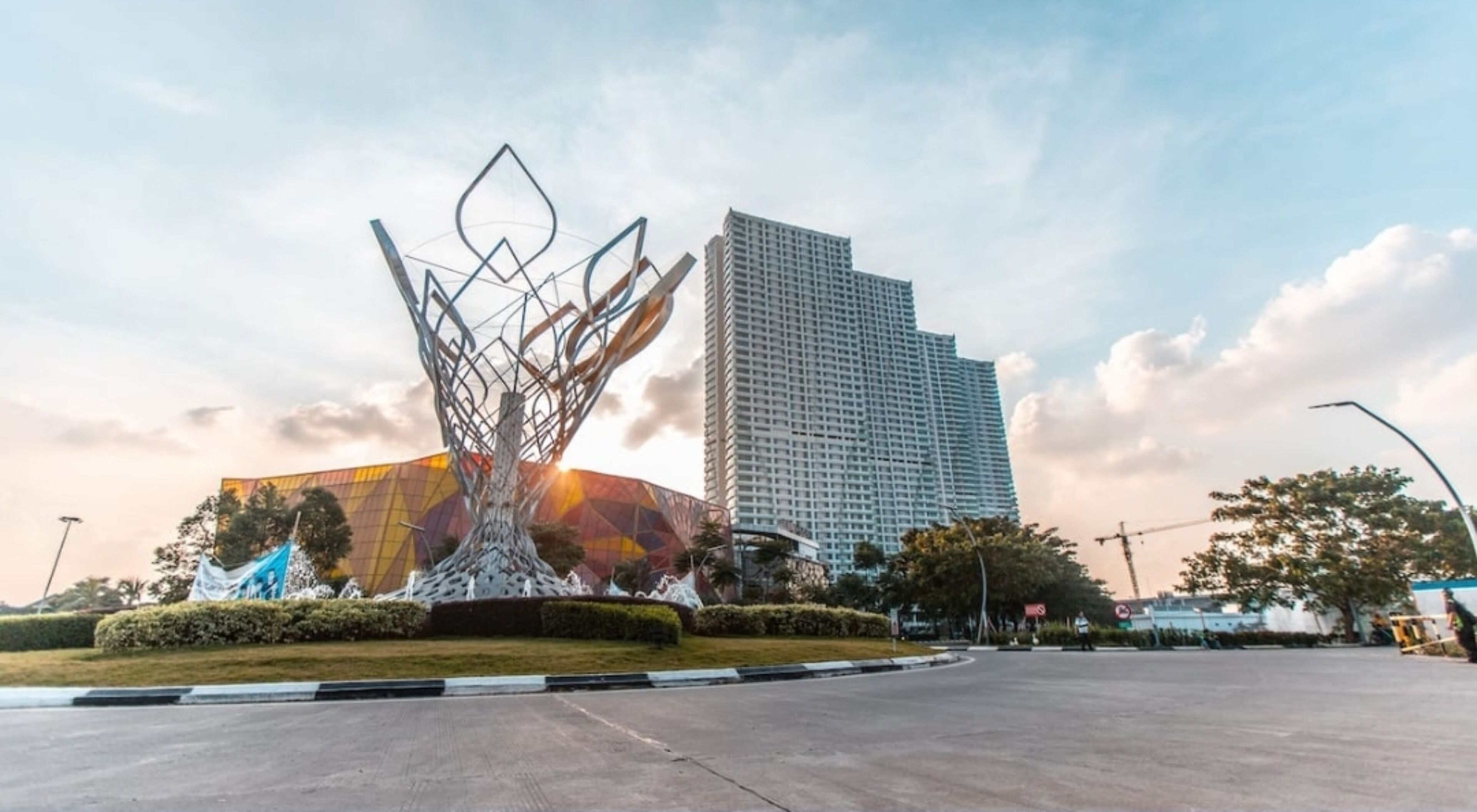 Una piazza moderna in città, con una grande scultura astratta in primo piano e un alto edificio rettangolare sullo sfondo.