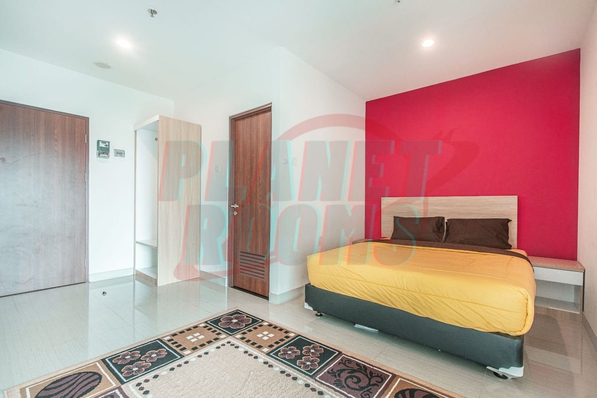 Une chambre à coucher avec un lit, un mur d’accent de couleur rouge et une porte en bois.