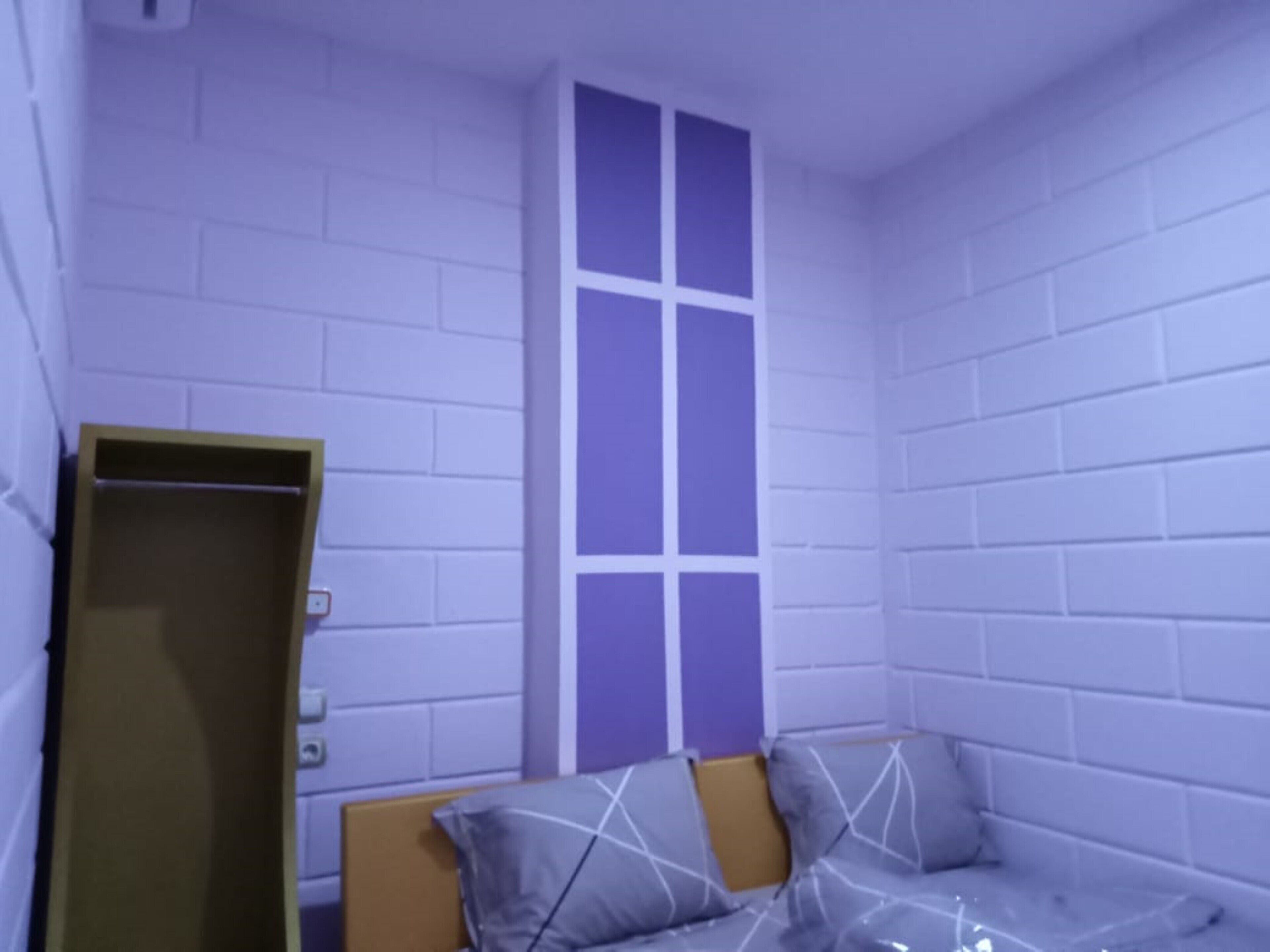 A room with white brick walls, a window, a bed with a headboard, and a wooden door.