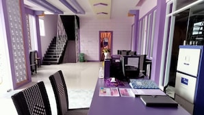 A reception area with a purple desk, black chairs, a staircase, and a view of the lobby. - Ungu Hotel Garut (Garut)