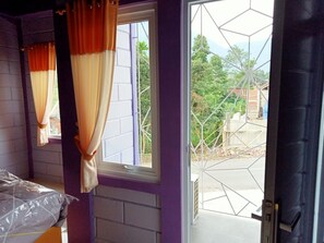 A room with a purple wall, a window with orange curtains, and a view of a geometric structure outside.