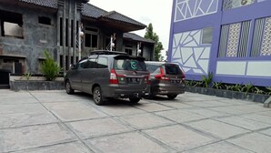 Two parked cars in front of a building with a tiled roof and a purple facade. - Ungu Hotel Garut (Garut)