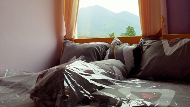 A room with a bed, a window with curtains, and a view of mountains. - Ungu Hotel Garut (Garut)