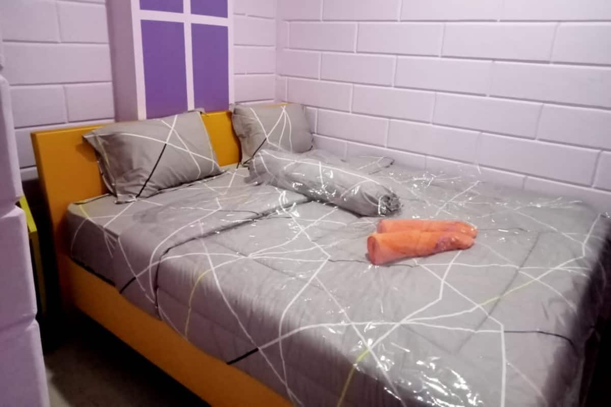 Uma cama de solteiro com um cobreleite cinza e branco estampado, cabeceira de madeira e almofada com padrão geométrico.