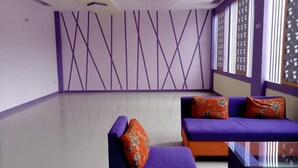 A modern room with purple and orange furniture, a patterned wall, and a large window with blinds. - Ungu Hotel Garut (Garut)