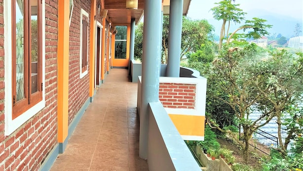 A corridor with brick walls and large windows, leading to a covered area with a view of greenery and a body of water. - Villa Orange Lembang Pengkolan (Lembang)