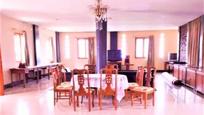 A dining area with a round table, multiple chairs, a chandelier, and a television on a stand. - Villa Orange Lembang Pengkolan (Lembang)