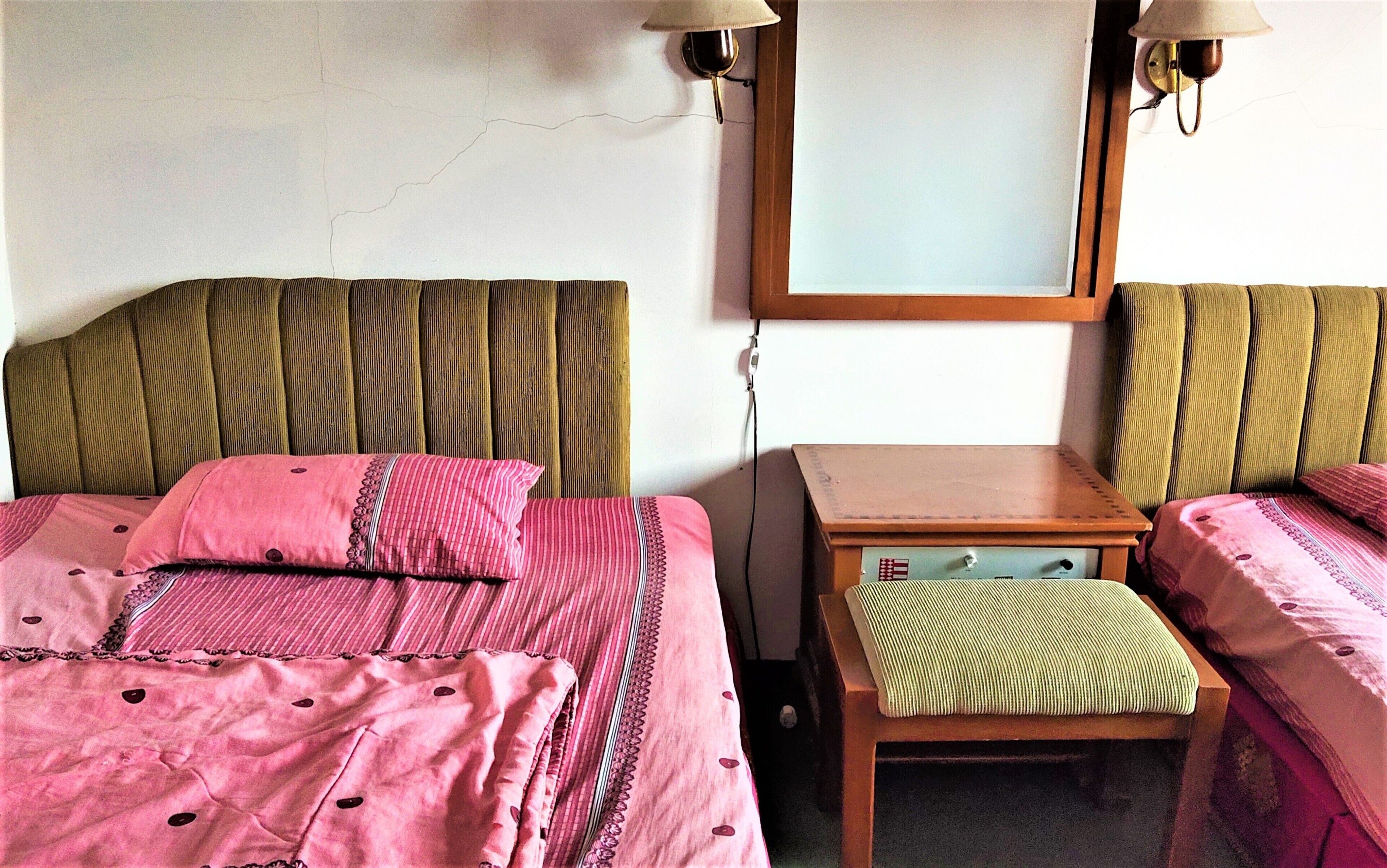 A hotel room with two beds, a small wooden table, and a mirror on the wall.