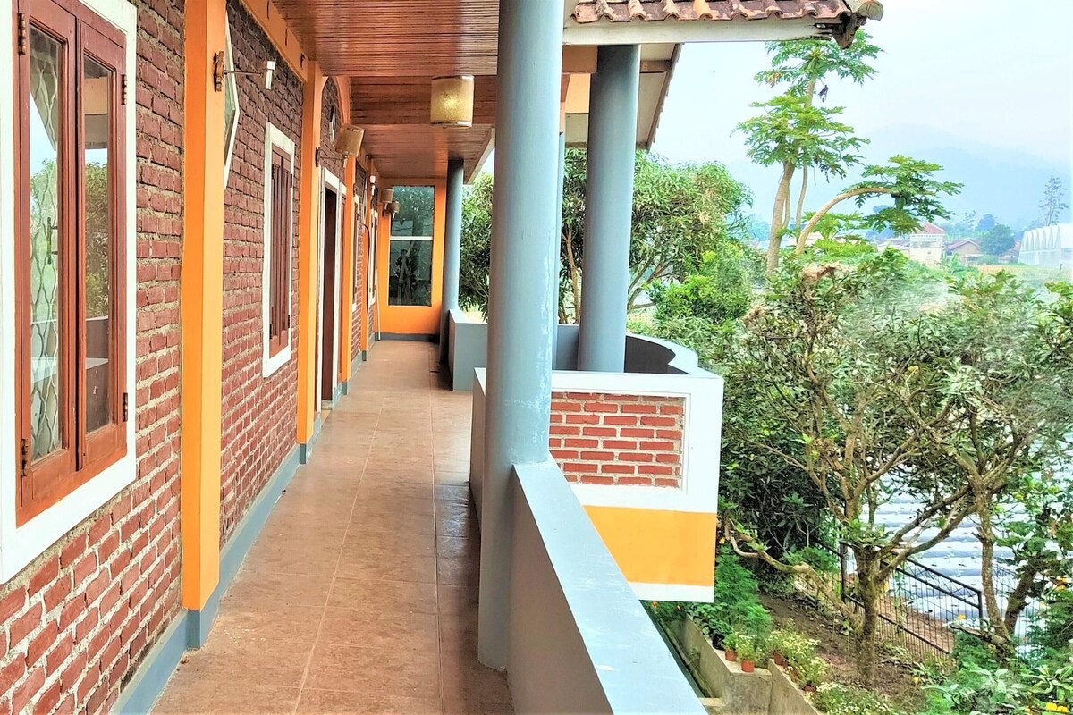 A covered balcony with brick walls and a tiled floor, overlooking a lush green area.