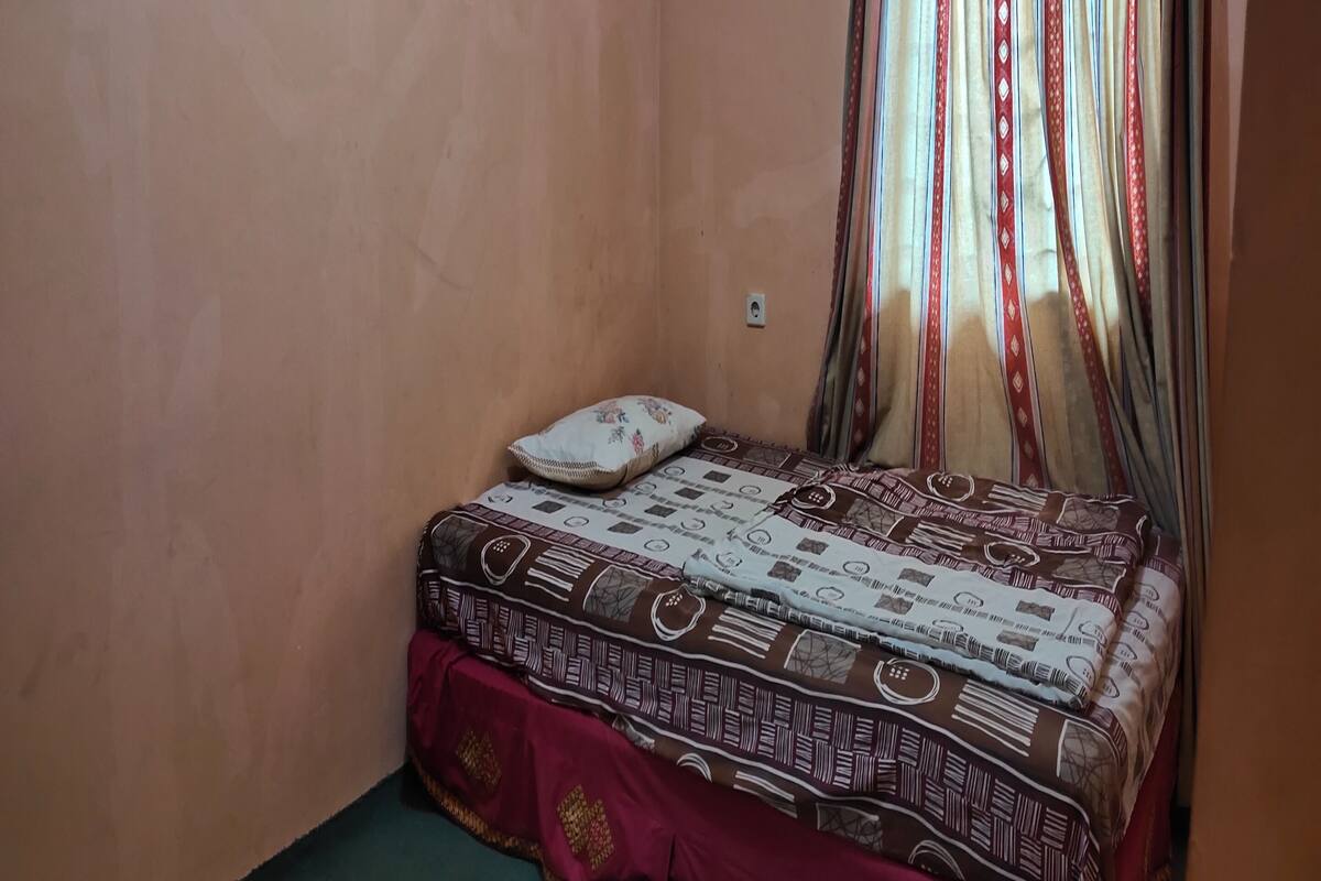 Une petite chambre avec un lit simple, une couvre-lit à motifs, un oreiller et des rideaux.