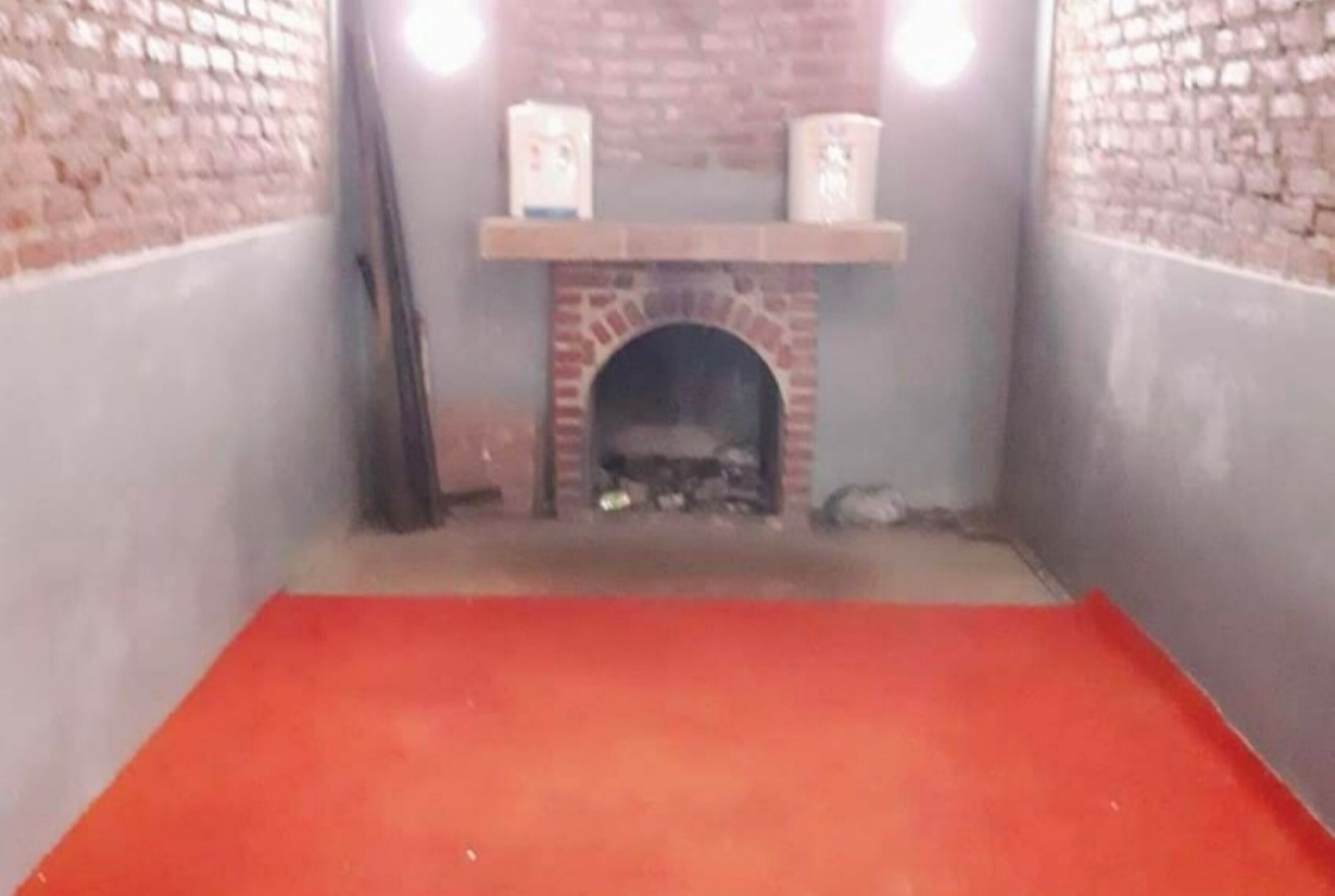 A room with a brick fireplace, a red carpet, and a shelf above the fireplace.