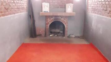A room with a brick fireplace, a red carpet, and a shelf above the fireplace.