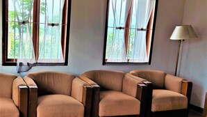 A room with three brown armchairs, a floor lamp, and two windows with curtains. - Villa Orange Lembang Pengkolan (Lembang)