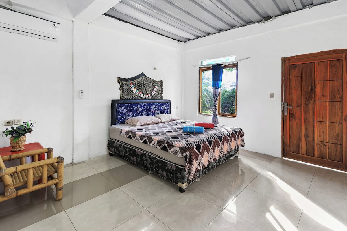 Een slaapkamer met een bed, een houten deur, een raam met gordijnen en een kleine tafel met een plant.