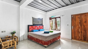 Une chambre à coucher avec un lit, une porte en bois, une fenêtre et une petite table sur laquelle est posée une plante.