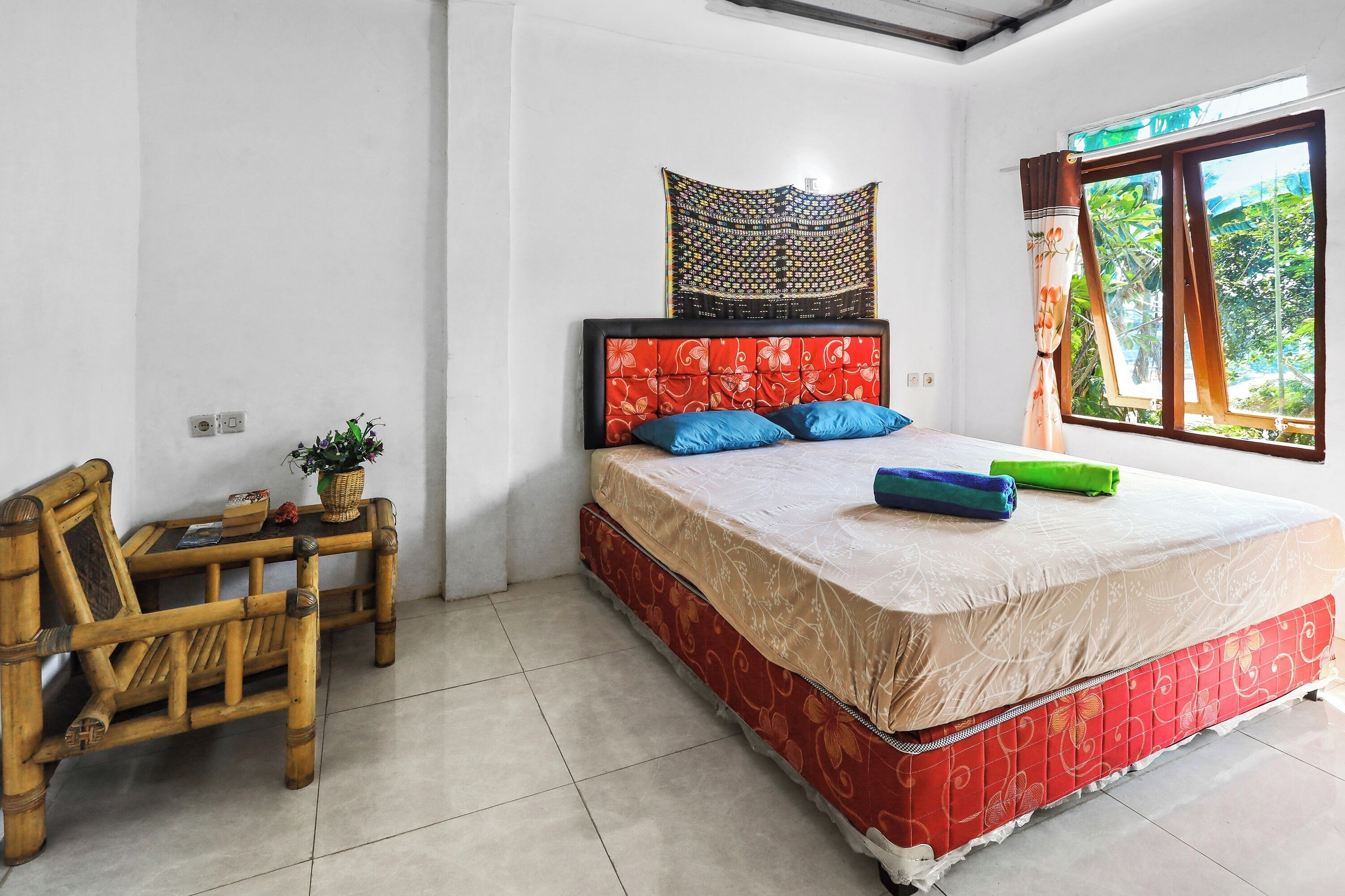 A bedroom with a bed, a chair, a small table, a tapestry, and a window with curtains.