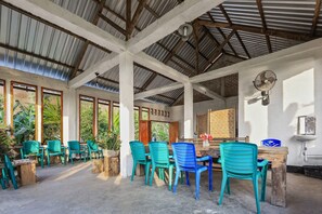 A covered outdoor dining area with wooden tables and chairs, surrounded by potted plants and a view of greenery. - Palulu Garden Homestay (Labuan Bajo)