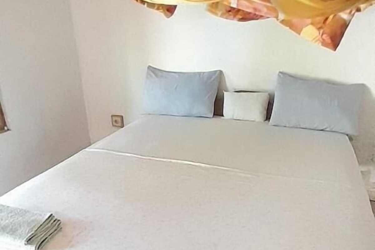 Un lit avec un matelas blanc, un cadre en bois et une tête de lit. Il y a des oreillers sur le lit et une couverture est posée sur la tête de lit.