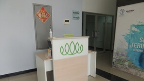 Un mostrador de recepción con un logo verde, un dispensador de gel hidroalcohólico y un cartel que indica la ubicación de los baños.