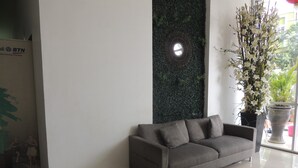 Un vestíbulo moderno con un sofá gris, un jardín vertical verde y un arreglo floral blanco en maceta.