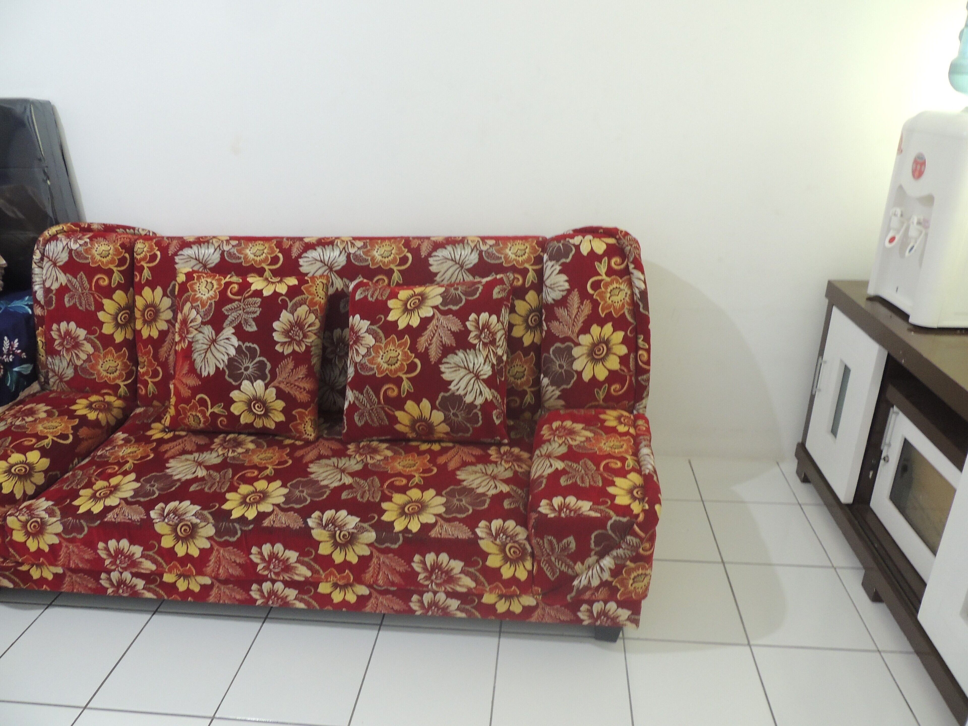 Un sofá rojo con estampado floral, un armario blanco y un microondas.