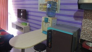Une pièce avec un mur à rayures violettes, un distributeur d’eau, un téléviseur et une table avec une chaise.