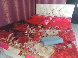 A bed with a floral bedspread, a white headboard, and red pillows.