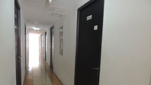 Un long couloir étroit, dont le sol est recouvert de carreaux, avec une porte noire sur la droite et une porte blanche sur la gauche.