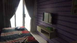 Une chambre d’hôtel avec un lit, des rideaux, un téléviseur posé sur un meuble et une fenêtre.