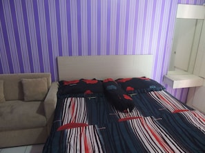 A bedroom with a bed, a sofa, and a bedside table with a mirror. - Alexandria Room at Apartement Paragon Village (Curug)