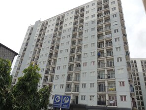 A high-rise apartment building with multiple balconies and a sign indicating directions to an apartment and a hotel. - Alexandria Room at Apartement Paragon Village (Curug)