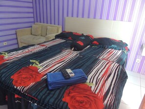 A bed with a striped bedspread, a remote control, and a folded blue towel. - Alexandria Room at Apartement Paragon Village (Curug)