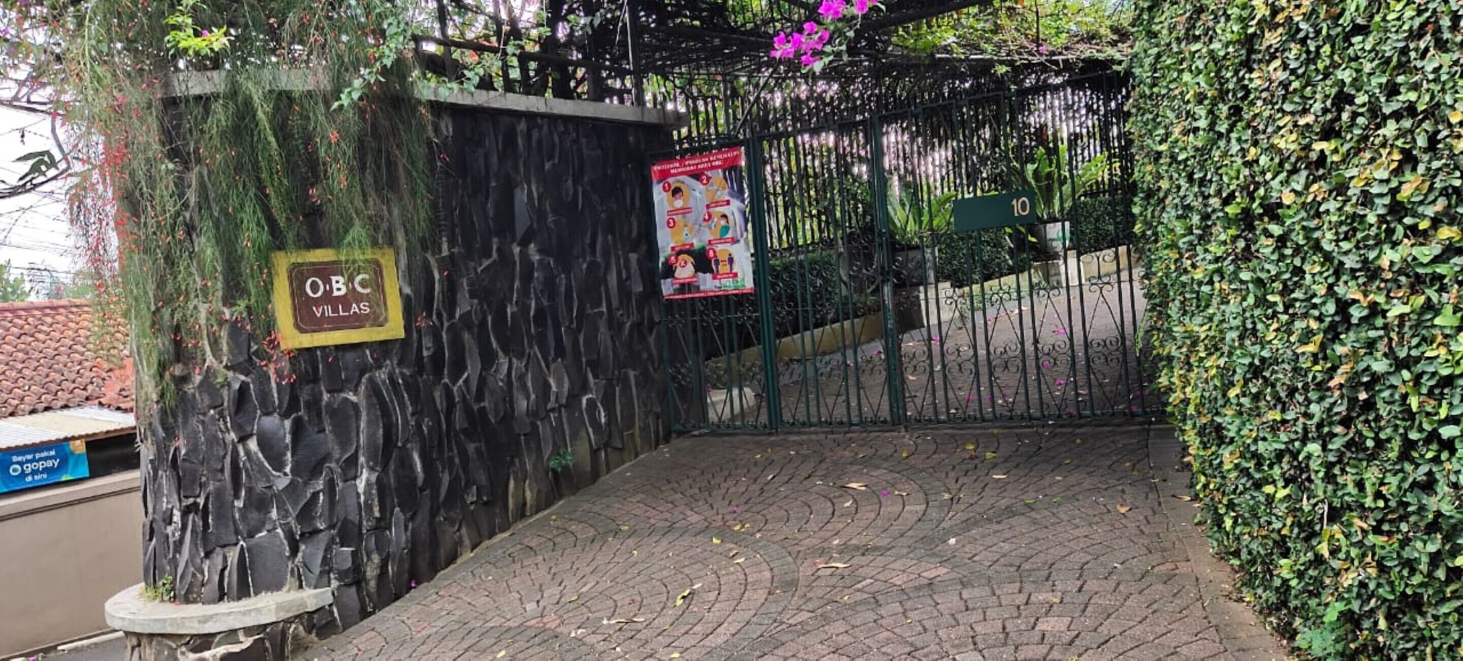 Une entrée fermée par un portail, agrémentée d’un panneau indiquant « OBC Villages », un mur en pierre et un chemin pavé.