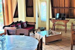 Un salon avec un canapé, une table basse, un téléviseur posé sur un meuble et une fenêtre avec des rideaux.